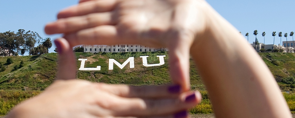 A student frames the Loyola Marymount University bluff letters in between his hands.